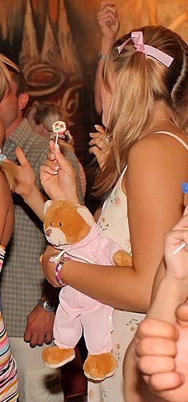 Teen girl at party with hair ribbons, lollipop and teddy bear in romper suit